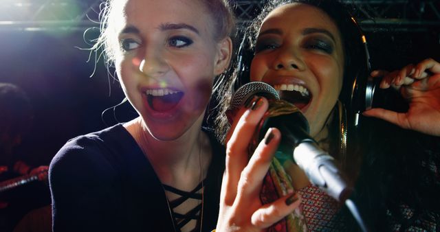 Two young Caucasian women are enjoying themselves singing into a microphone, with vibrant lighting highlighting their excitement. Their joyful expressions and the dynamic atmosphere suggest they are having a great time at a karaoke event or a lively party.