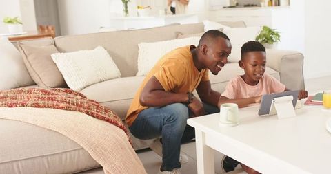 Father and son watching tablet together in cozy living room, bonding and learning