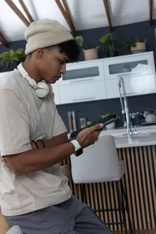 African american man using tablet in minimalist kitchen wearing headphones and smartwatch