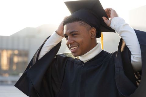 African american teen smiling, adjusting graduation cap in black gown with gold tassel