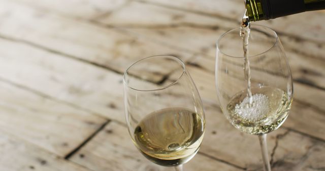 Two glasses on rustic wooden table being filled with white wine, ideal for themes related to celebrating, relaxing, fine dining, or promoting wine brands. Perfect for advertisements, social media posts, blog articles on wine tasting or luxury nibbles, or even restaurant menus.