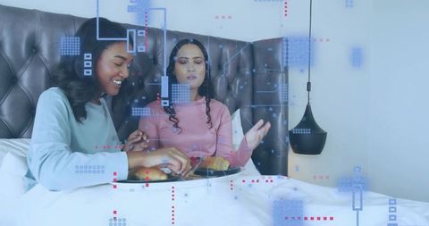 Sharing breakfast in bed with AR overlays, two women enjoying cozy digital morning