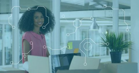 Smiling professional woman at modern open-plan desk with laptop, boxes and plant