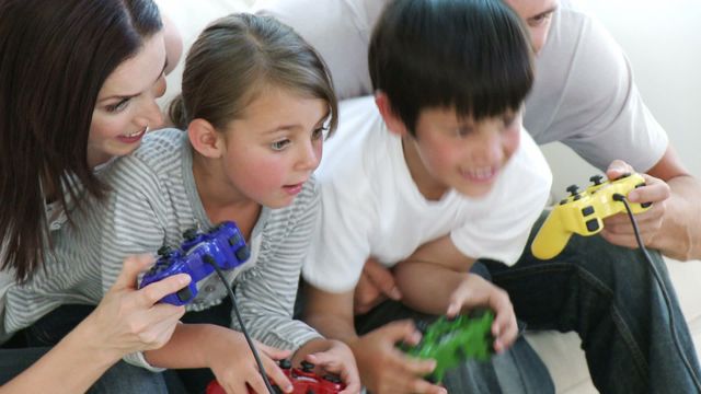 Family gathered in cozy living room, engaged in gaming session with controllers. Captures fun and bonding moments. Ideal for use in advertisements related to family activities, gaming products, or lifestyle articles emphasizing family time and entertainment at home.