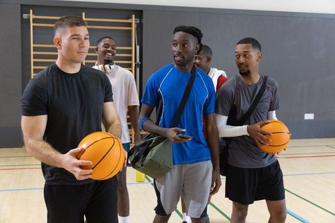 Multiethnic male basketball teammates chatting and holding balls on indoor court