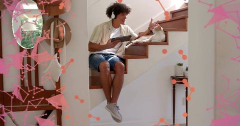 Young man petting cat on stairs while using tablet and wearing headphones