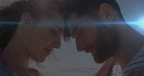 Romantic couple pressing foreheads together amidst lens flare on beach