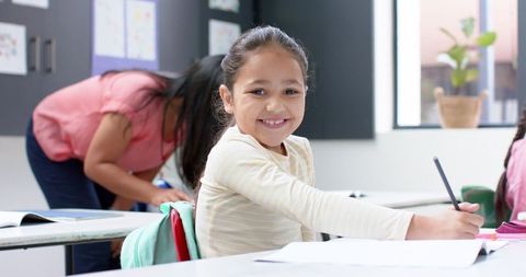 Smiling schoolgirl writing in classroom setting