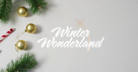 Winter wonderland lettering framing gold baubles and pine sprigs on minimal pale surface