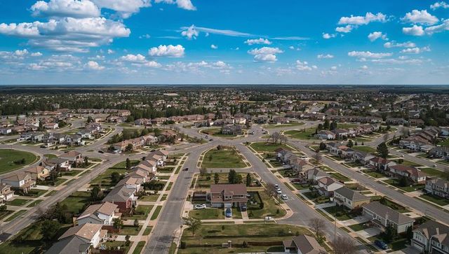 Aerial overlooking suburban neighborhood with central two-story home and roundabout
