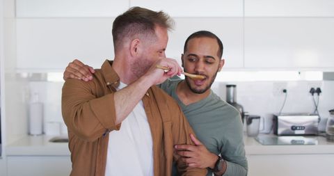 Happy Same-Sex Couple Cooking and Tasting in Modern Kitchen