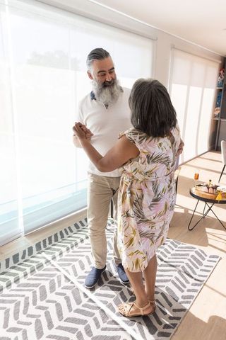 Senior couple dancing in sunlit living room embracing, cozy intimate home moment