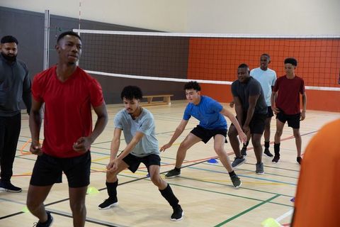 Diverse male volleyball players practicing defensive footwork during indoor training drill
