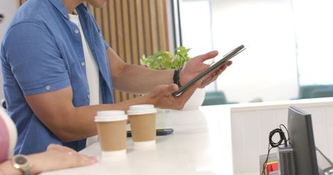 Man using tablet at bright cafe counter with coffee cups for mobile ordering promotion