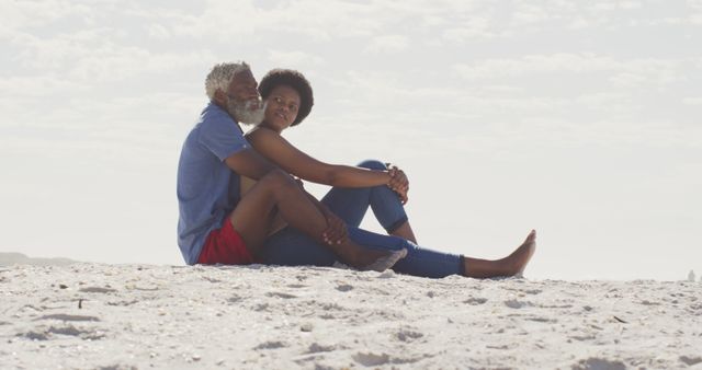 Happy african american couple sitting and embracing on sunny beach. healthy and active time beach holiday.