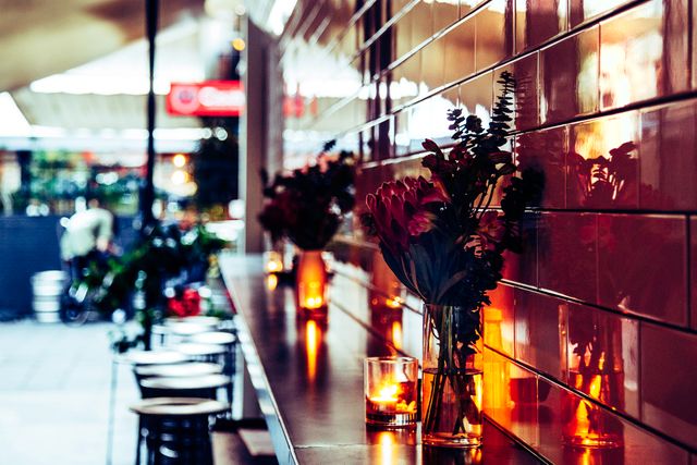 Warm urban café interior is ideal for projects related to lifestyle, city living, and hospitality. Flowers in vase and soft lighting create inviting ambiance, perfect for articles or ads focused on relaxing evening spots, intimate gatherings, or showcasing modern café designs.