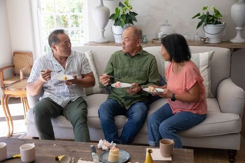 Chinese multigenerational family sharing cake on sofa in cozy sunlit living room