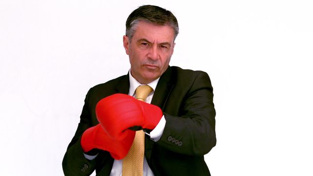 Mature businessman wearing suit and boxing gloves displays readiness to face challenges head-on. Image ideal for themes centered on corporate strength, leadership, competition, and motivational content. Useful in business presentations, blog posts about overcoming obstacles, or illustrations for competitive strategy articles.