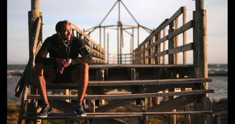 Young Male Jogger Relaxing on Wooden Pier Near Beach - Download Free Stock Images Pikwizard.com