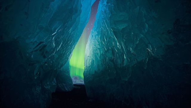 Framing narrow ice cave passage revealing green aurora through crystalline glacier slit