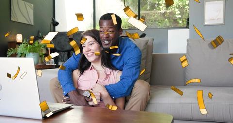 Joyful couple embracing on couch with laptop while gold confetti falls celebrating online win