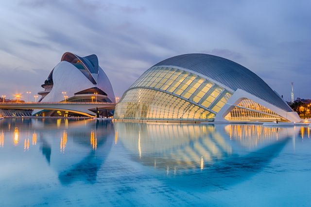 Colorful, nighttime view of gleaming modern buildings at the City of Arts and Sciences in Valencia, Spain, showcases futuristic architectural designs and serene water reflections. Ideal for use in travel brochures, architecture magazines, and educational materials highlighting modern European landmarks and futuristic designs.