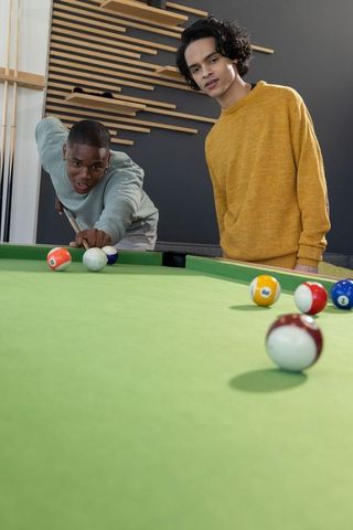African american and asian friends playing pool on green-felt table in modern lounge