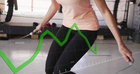Jumping female athlete holding jump rope with green analytics overlay in boxing gym