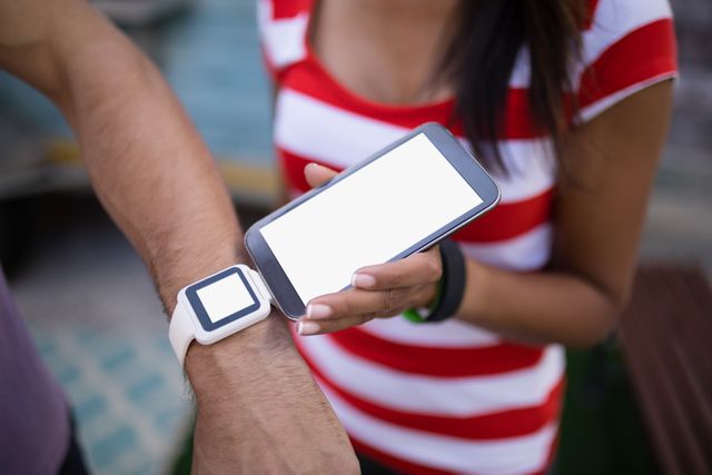 Close-up of a man paying a bill using a smartwatch, with a woman holding a smartphone. Ideal for illustrating modern payment methods, fintech innovations, and the convenience of contactless transactions. Suitable for use in articles, blogs, and advertisements related to technology, finance, and digital wallets.