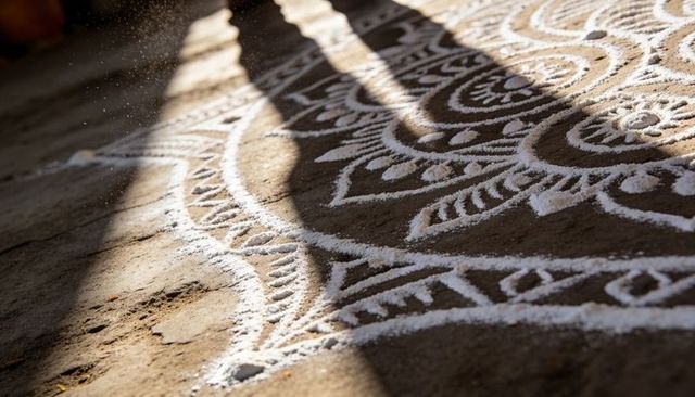 Sunlit white rangoli powder on rustic courtyard floor casting long diagonal shadows