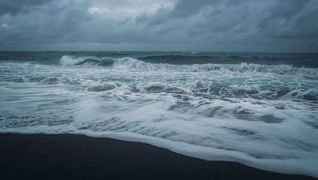 Stormy ocean waves rolling and crashing over dark sand shoreline under overcast sky
