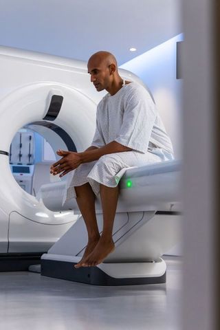 African man sitting on mri table in radiology clinic wearing patient gown