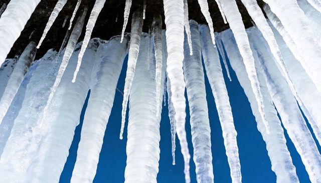 Hanging icicles showcasing layered ridges and dripping droplets against deep blue sky