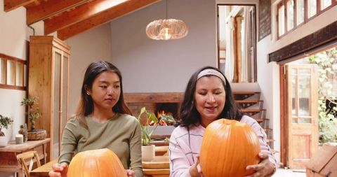 Mother Daughter Preparing Pumpkins on Rustic Wooden Table by Fireplace for Autumn Harvest