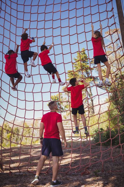 Trainer guiding kids climbing a net in an outdoor obstacle course. Ideal for illustrating teamwork, physical activity, and outdoor adventure. Suitable for use in educational materials, fitness programs, summer camp promotions, and articles on children's sports and exercise.