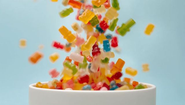 Colorful gummy bears pouring into white ceramic bowl