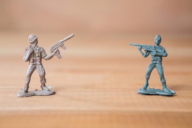 Two miniature army soldiers are positioned as if in battle on a wooden surface. One soldier is gray and the other is green, both holding rifles. This image can be used for themes related to childhood play, military strategy games, or toy collections. It is ideal for illustrating concepts of combat, strategy, and military-themed activities.