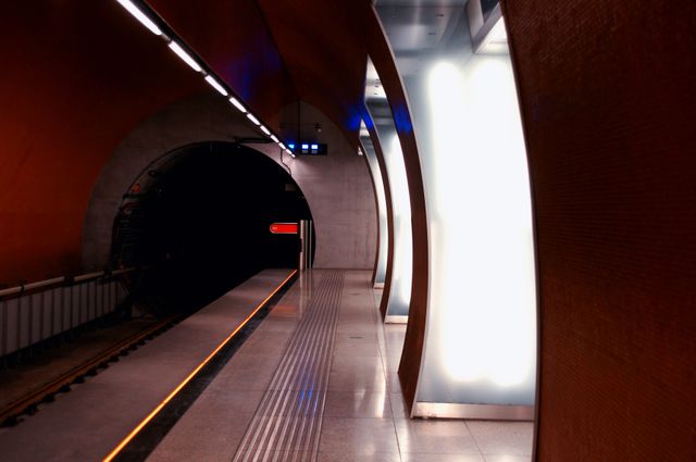 Empty subway platform with illuminated columns and curved architecture. Tunnel leads into darkness, showing modern urban transportation setting. Suitable for topics on city life, public transit, infrastructure, urban exploration, and travel.