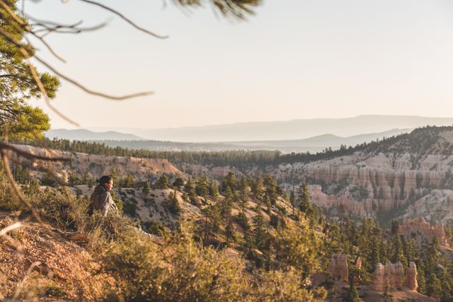 Person sitting on the edge while watching the sunset over Bryce Canyon's stunning rock formations and forested terrain. Perfect for travel blogs, outdoor adventure, nature photography, and relaxation-themed content.