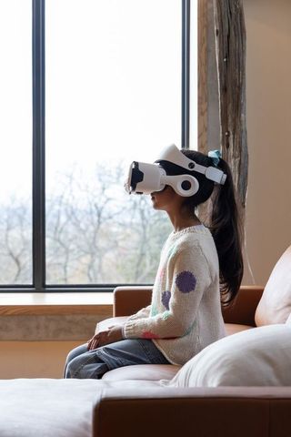 Asian Girl Wearing VR Headset Sitting on Sofa by Window Exploring Virtual World