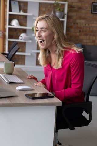 Excited Businesswoman at Desk Reacting to Computer in Modern Office