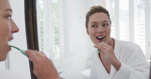 Smiling Woman Brushing Teeth in Bathroom Mirror Reflection