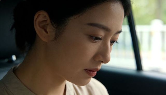 Introspective asian woman looking downward in car wearing beige collared top closeup portrait