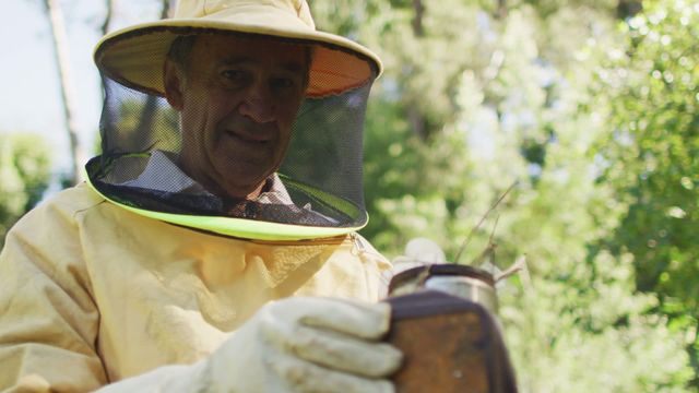 This video shows a Caucasian male beekeeper dressed in protective clothing while using a smoker to calm bees. It can be used for articles, blogs, or educational materials on beekeeping, small-scale farming, honey production, and sustainable agricultural practices. It illustrates human interaction with nature and the importance of safety measures in beekeeping.