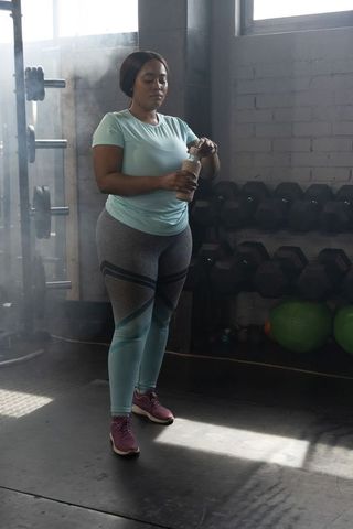 African american woman drinking from shaker during strength training in industrial gym