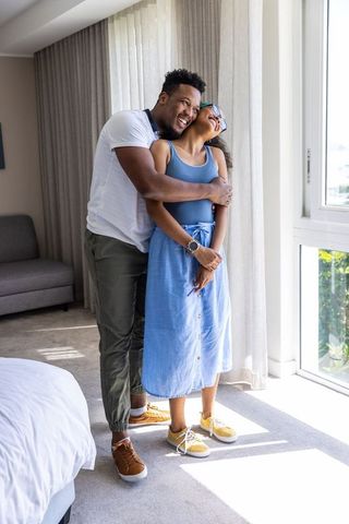 Sunlit romantic embrace between african american couple in modern hotel-style bedroom