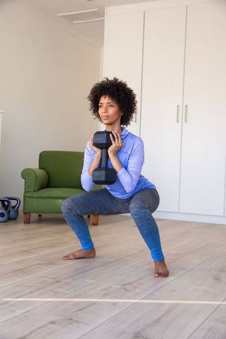 Focused Young Woman Performing Dumbbell Squats in Living Room