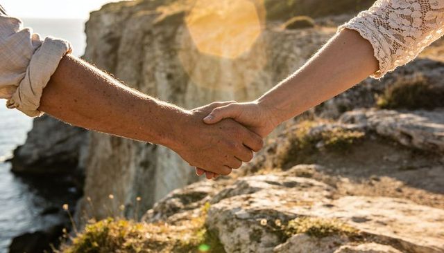 Sunlit couple holding hands on rugged coastal cliff, romance and partnership