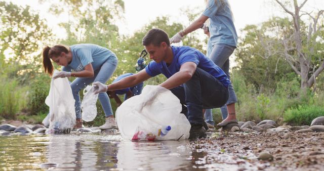 Group of volunteers collecting trash from riverbank promoting environment conservation. Ideal for usage in community service initiatives, eco-friendly projects, conservation awareness campaigns, and advertisements promoting nature clean-up activities. Highlights teamwork, youthful energy, and dedication to a cleaner environment.