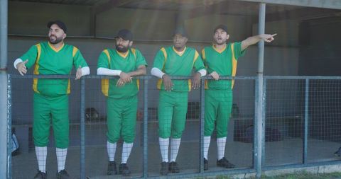 Baseball teammates leaning on dugout railing pointing and rallying in green uniforms